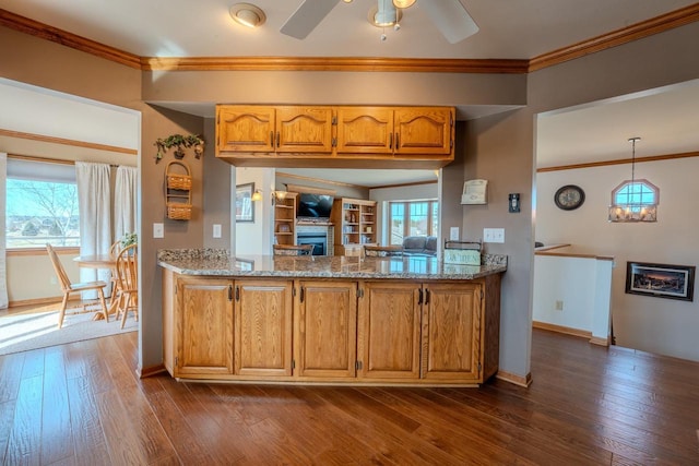 kitchen featuring dark wood-style floors, a ceiling fan, a fireplace, crown molding, and brown cabinets