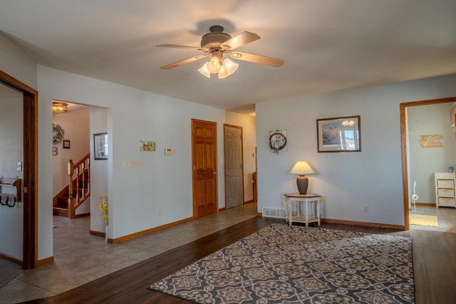 living area with visible vents, baseboards, stairs, wood finished floors, and a ceiling fan