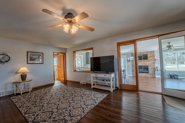 living area featuring a stone fireplace, wood finished floors, baseboards, and ceiling fan