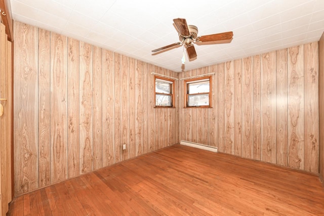 empty room with a baseboard heating unit, wooden walls, wood finished floors, and ceiling fan