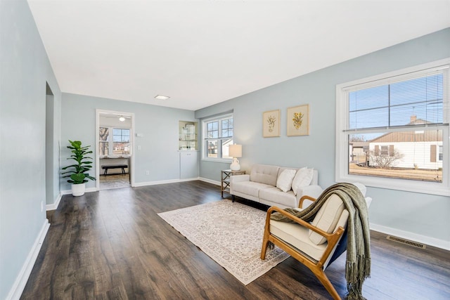 living area featuring visible vents, a healthy amount of sunlight, baseboards, and dark wood-style flooring