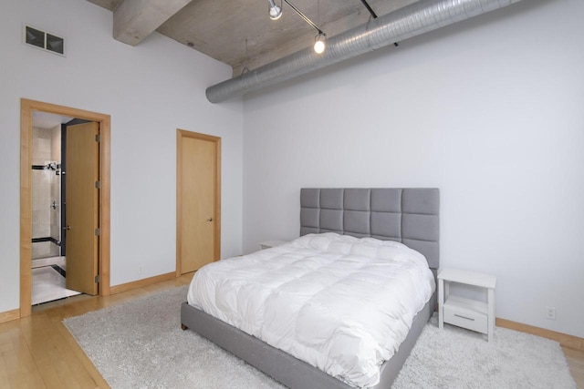 bedroom with rail lighting, wood finished floors, visible vents, and baseboards