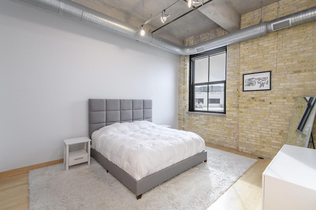 bedroom featuring wood finished floors, visible vents, brick wall, and baseboards