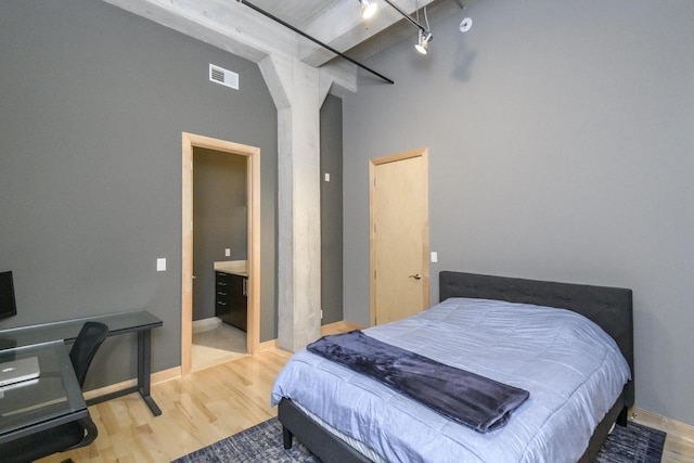 bedroom with visible vents, track lighting, a high ceiling, and wood finished floors