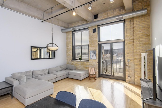 living room featuring rail lighting, wood finished floors, a towering ceiling, and brick wall