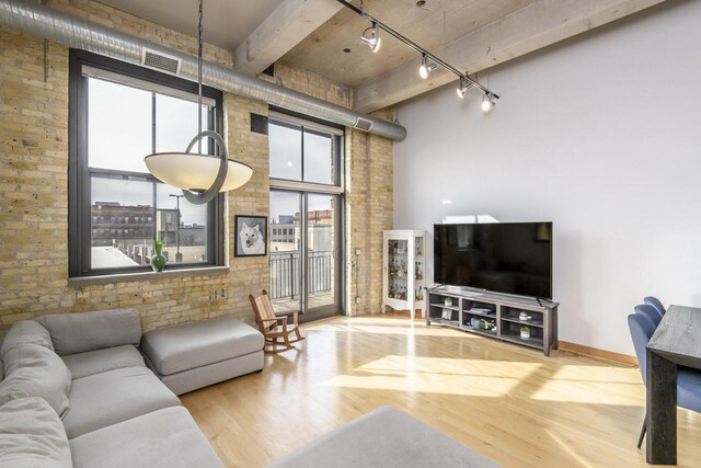 living room with visible vents, track lighting, wood finished floors, a high ceiling, and brick wall