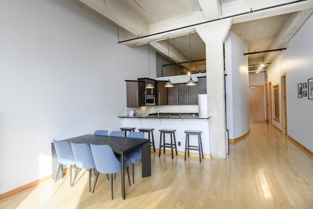 dining area with light wood-type flooring, baseboards, and a towering ceiling