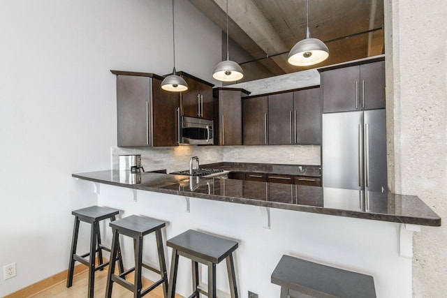 kitchen with light wood-style flooring, backsplash, stainless steel appliances, a peninsula, and dark brown cabinets