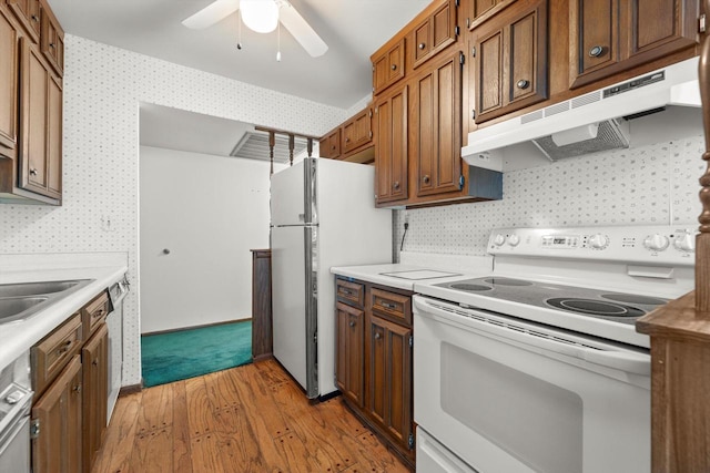 kitchen featuring under cabinet range hood, white appliances, light countertops, and light wood-style floors