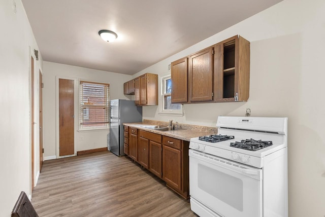 kitchen featuring open shelves, white range with gas cooktop, freestanding refrigerator, light wood-style floors, and a sink