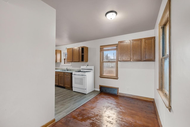 kitchen featuring visible vents, white range with gas cooktop, brown cabinets, wood finished floors, and baseboards