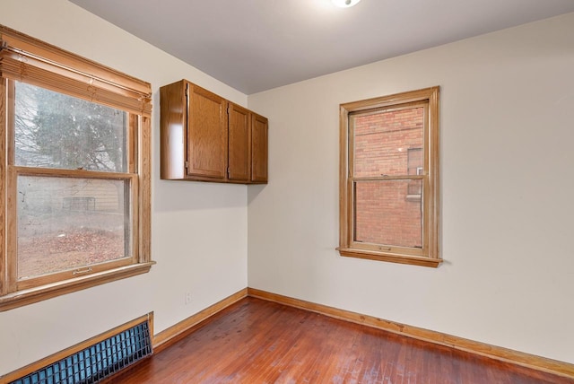 spare room featuring wood finished floors, a healthy amount of sunlight, baseboards, and visible vents