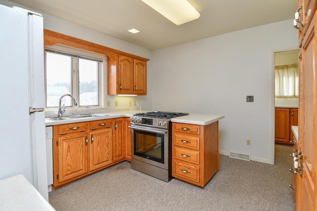 kitchen with brown cabinetry, freestanding refrigerator, a sink, light countertops, and gas range