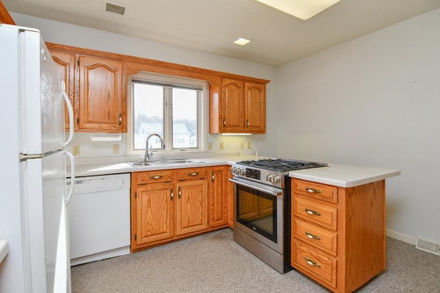 kitchen with brown cabinets, a sink, white appliances, a peninsula, and light countertops