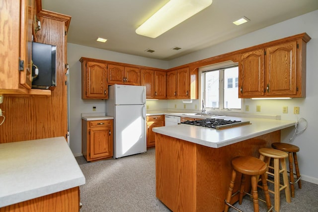 kitchen with white appliances, brown cabinetry, a peninsula, and light countertops