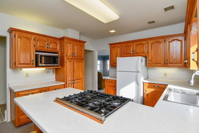 kitchen with stainless steel microwave, visible vents, stovetop, freestanding refrigerator, and a sink