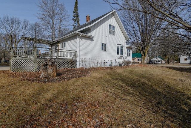 view of property exterior featuring a yard, a deck, and a chimney