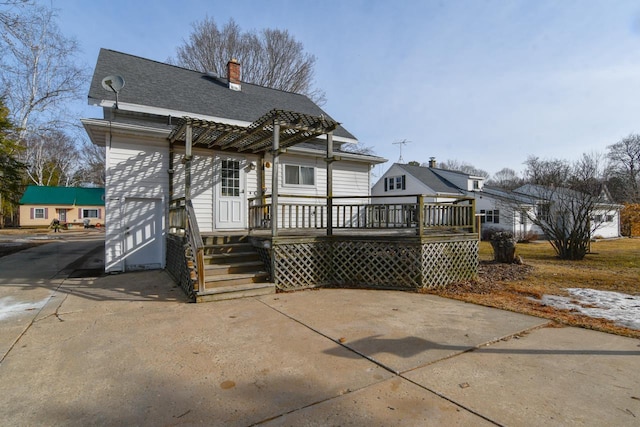 rear view of house featuring a shingled roof, a wooden deck, and a chimney