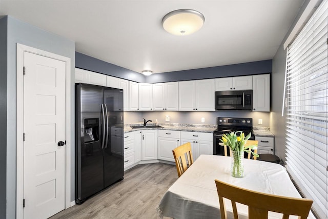 kitchen featuring light wood-type flooring, black fridge, stainless steel microwave, electric range oven, and white cabinets