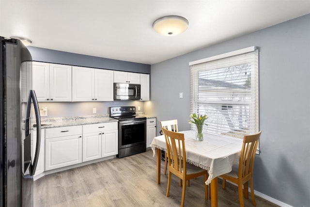 kitchen with light wood finished floors, appliances with stainless steel finishes, white cabinetry, and baseboards