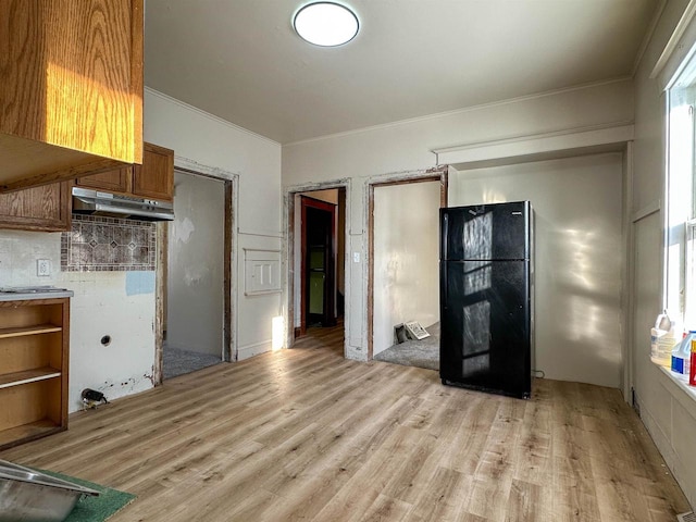 kitchen featuring backsplash, light wood-type flooring, ornamental molding, brown cabinets, and freestanding refrigerator