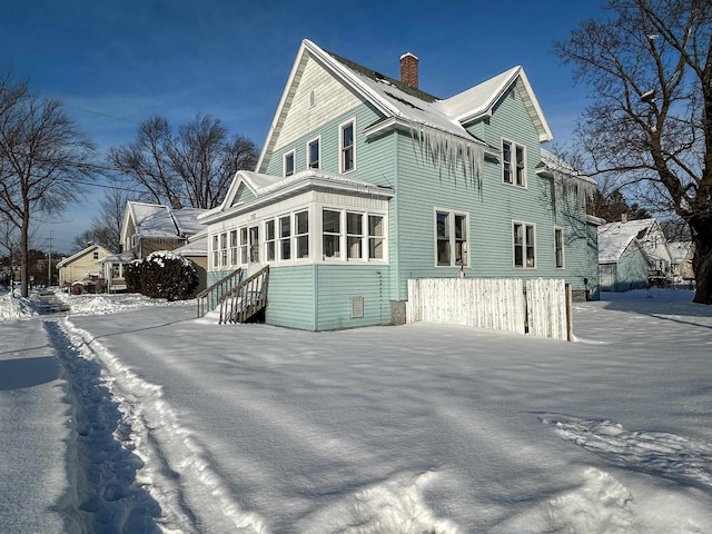 view of snow covered exterior featuring a chimney and a sunroom