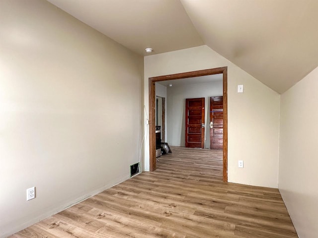 hallway with visible vents, lofted ceiling, and light wood-style floors