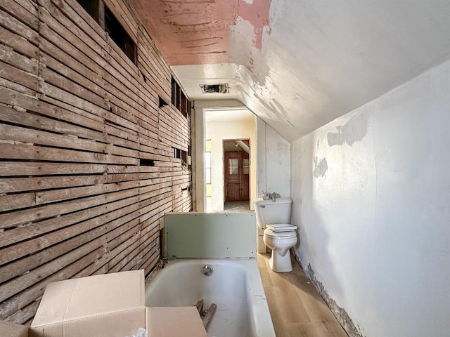 bathroom featuring wood walls, toilet, vaulted ceiling, a bathing tub, and wood finished floors