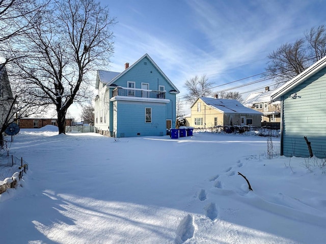 snow covered back of property with a chimney and a balcony