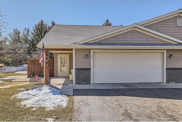 view of front of house with aphalt driveway, fence, a shingled roof, a garage, and brick siding