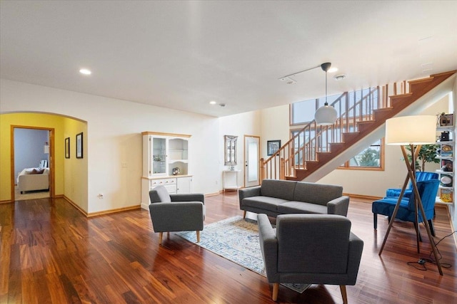 living area with stairs, wood finished floors, baseboards, and arched walkways