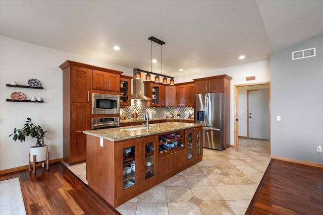 kitchen with visible vents, light stone countertops, brown cabinetry, stainless steel appliances, and wall chimney exhaust hood