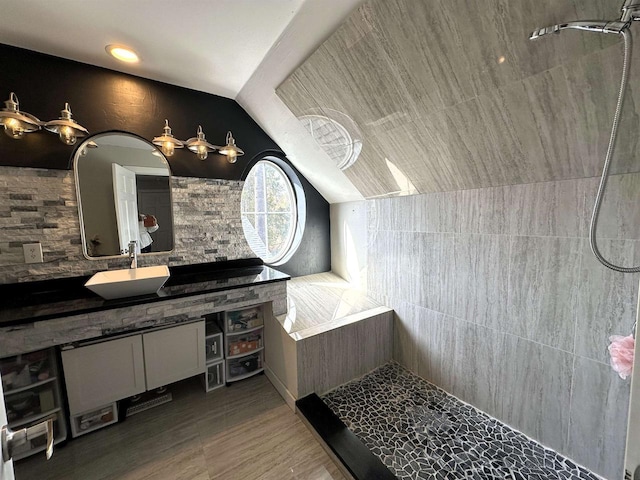 bathroom featuring wood finished floors, decorative backsplash, tiled shower, vanity, and vaulted ceiling