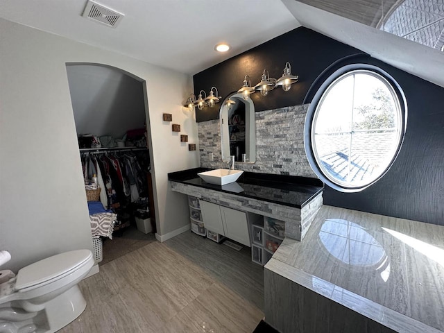 full bath with vanity, visible vents, lofted ceiling, a walk in closet, and toilet