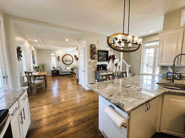 kitchen with light stone counters, dark wood finished floors, a sink, open floor plan, and tasteful backsplash