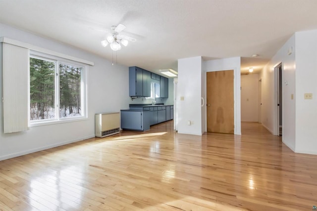 unfurnished living room featuring a sink, baseboards, light wood-style flooring, and ceiling fan