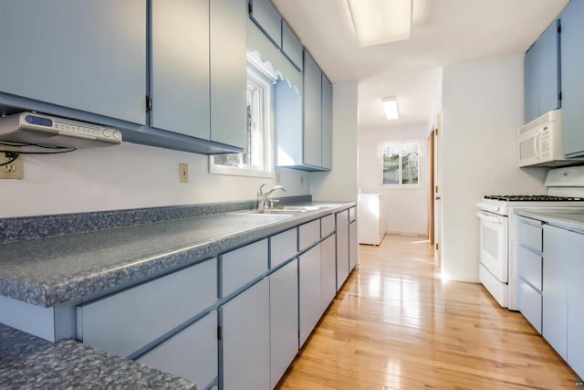 kitchen with blue cabinetry, a wealth of natural light, light wood-style floors, white appliances, and a sink