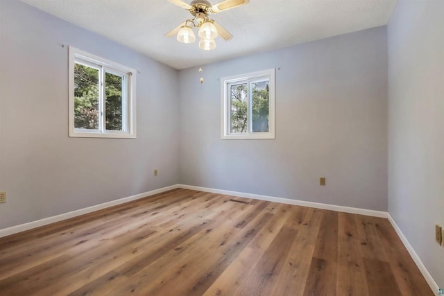 spare room featuring a wealth of natural light, baseboards, wood finished floors, and a ceiling fan