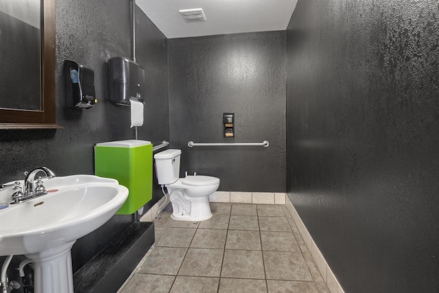 bathroom featuring tile patterned floors, baseboards, toilet, and a textured wall