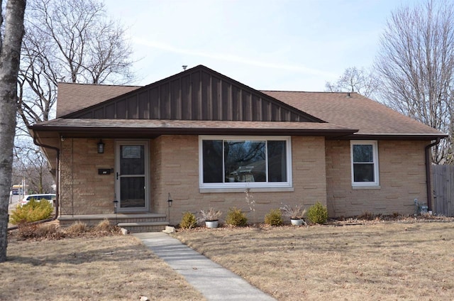 view of front of home with board and batten siding, brick siding, roof with shingles, and a front lawn