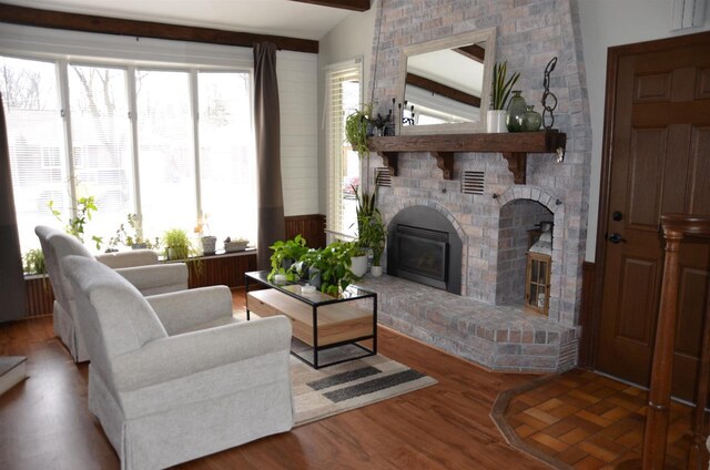 living room with a brick fireplace, lofted ceiling with beams, and wood finished floors