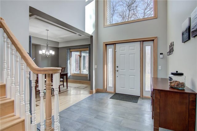 foyer entrance with stairway, baseboards, a chandelier, and a towering ceiling