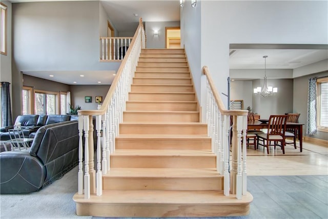 stairway with a notable chandelier, a towering ceiling, and wood finished floors