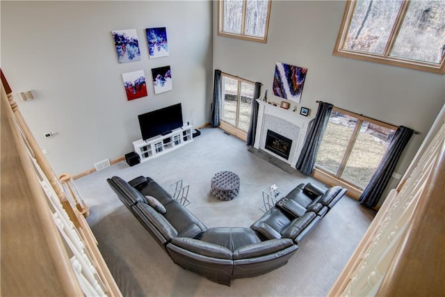 carpeted living room featuring plenty of natural light, a high ceiling, and a glass covered fireplace