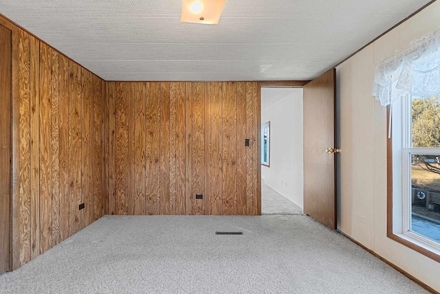 unfurnished room with a wealth of natural light, carpet flooring, and wood walls