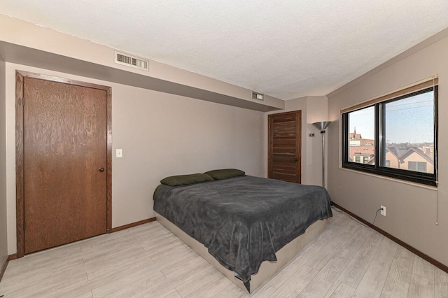 bedroom with light wood-type flooring, visible vents, baseboards, and a textured ceiling