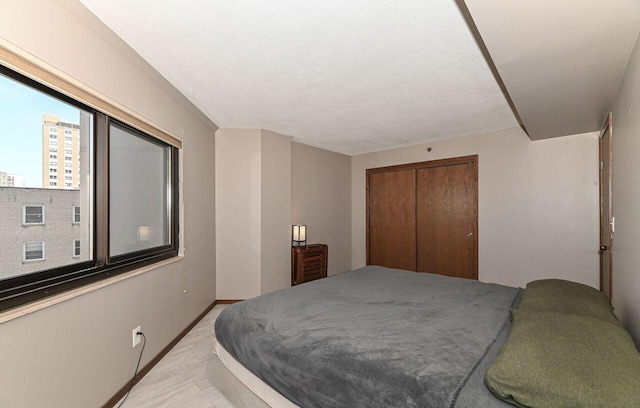 bedroom with a textured ceiling, baseboards, a closet, and light wood-type flooring