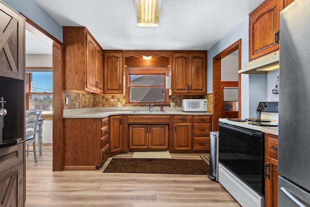 kitchen with white microwave, range with electric cooktop, under cabinet range hood, freestanding refrigerator, and a sink