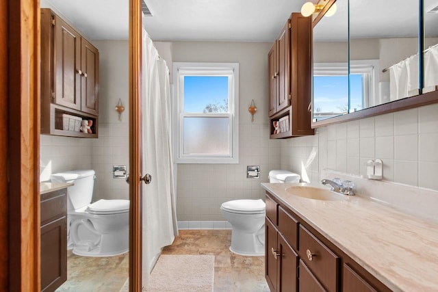 full bathroom featuring vanity, tile walls, toilet, and visible vents