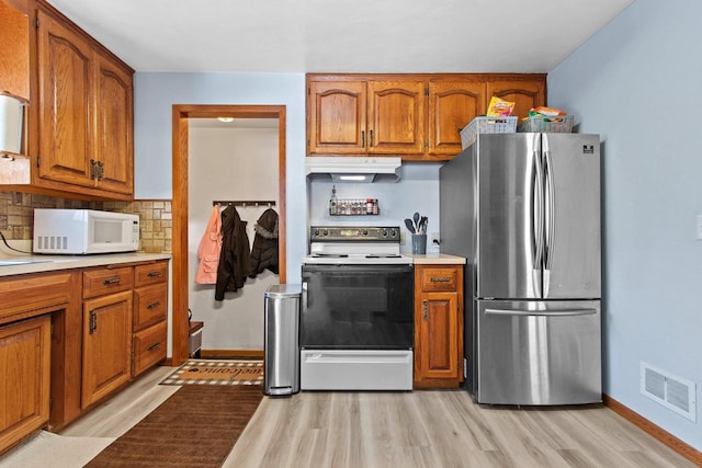 kitchen featuring visible vents, range with electric cooktop, under cabinet range hood, freestanding refrigerator, and white microwave